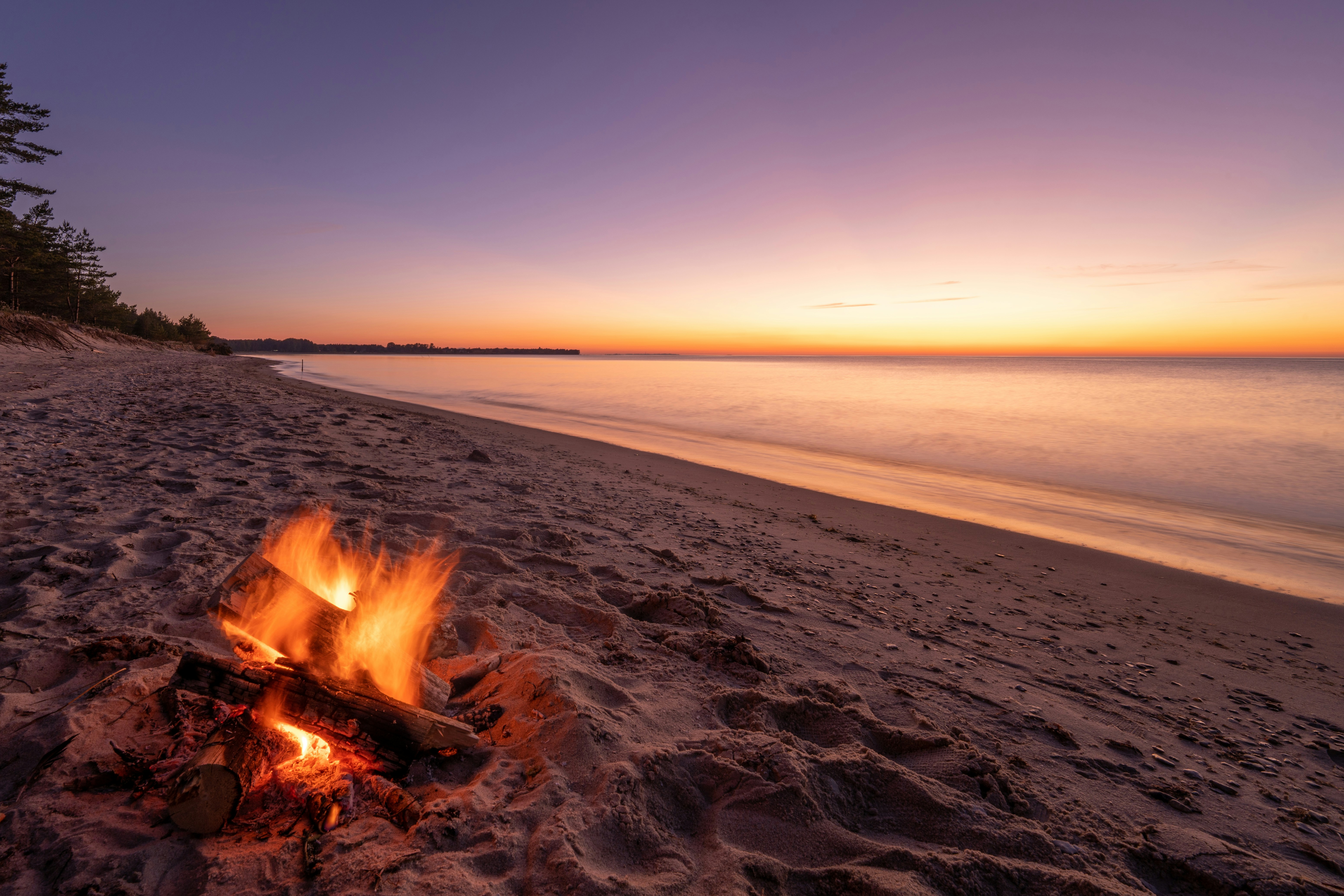 A campfire on a peaceful shoreline at sunset